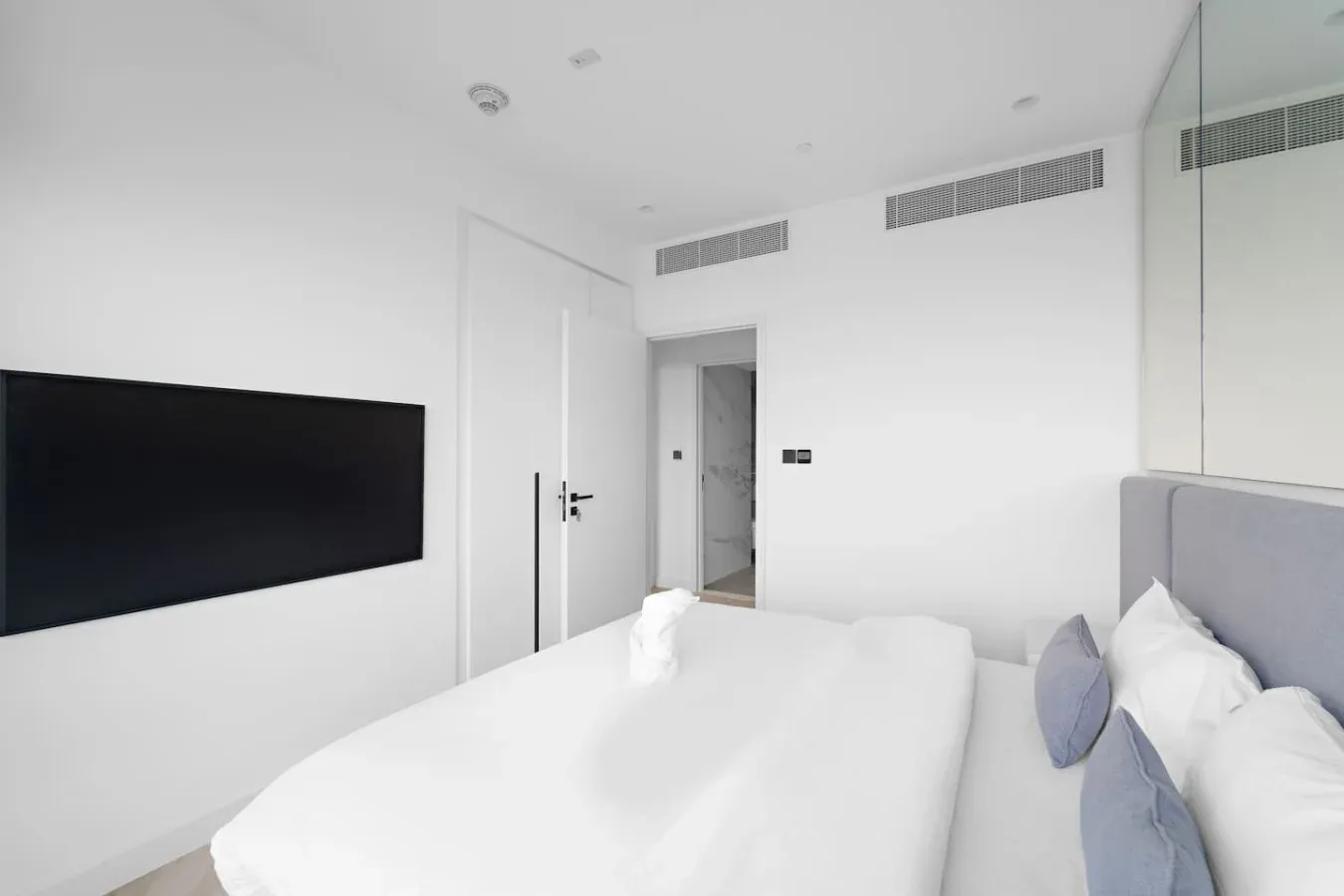 Un dormitorio luminoso con una cama y un televisor montado en la pared.