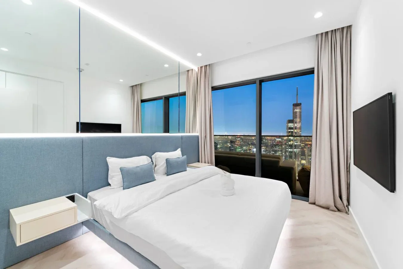 Un dormitorio luminoso con una cama bien arreglada y grandes ventanales con vistas a la ciudad.