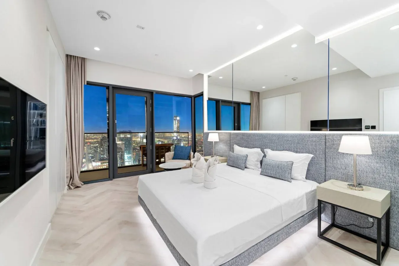 Un dormitorio luminoso con una cama grande frente a ventanales con vistas a la ciudad.