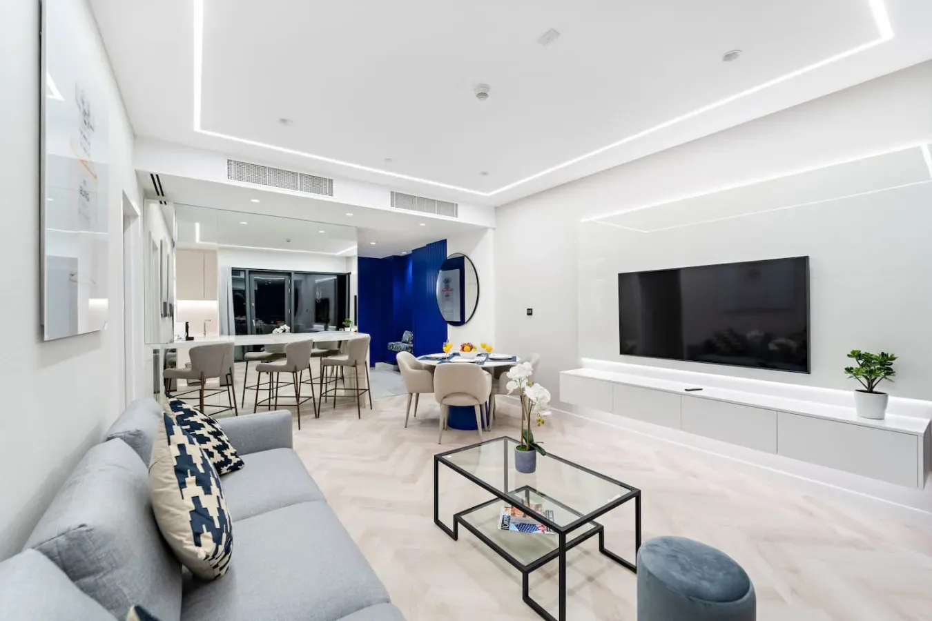 Una sala luminosa con asientos, una mesa de centro de vidrio y un televisor en la pared.