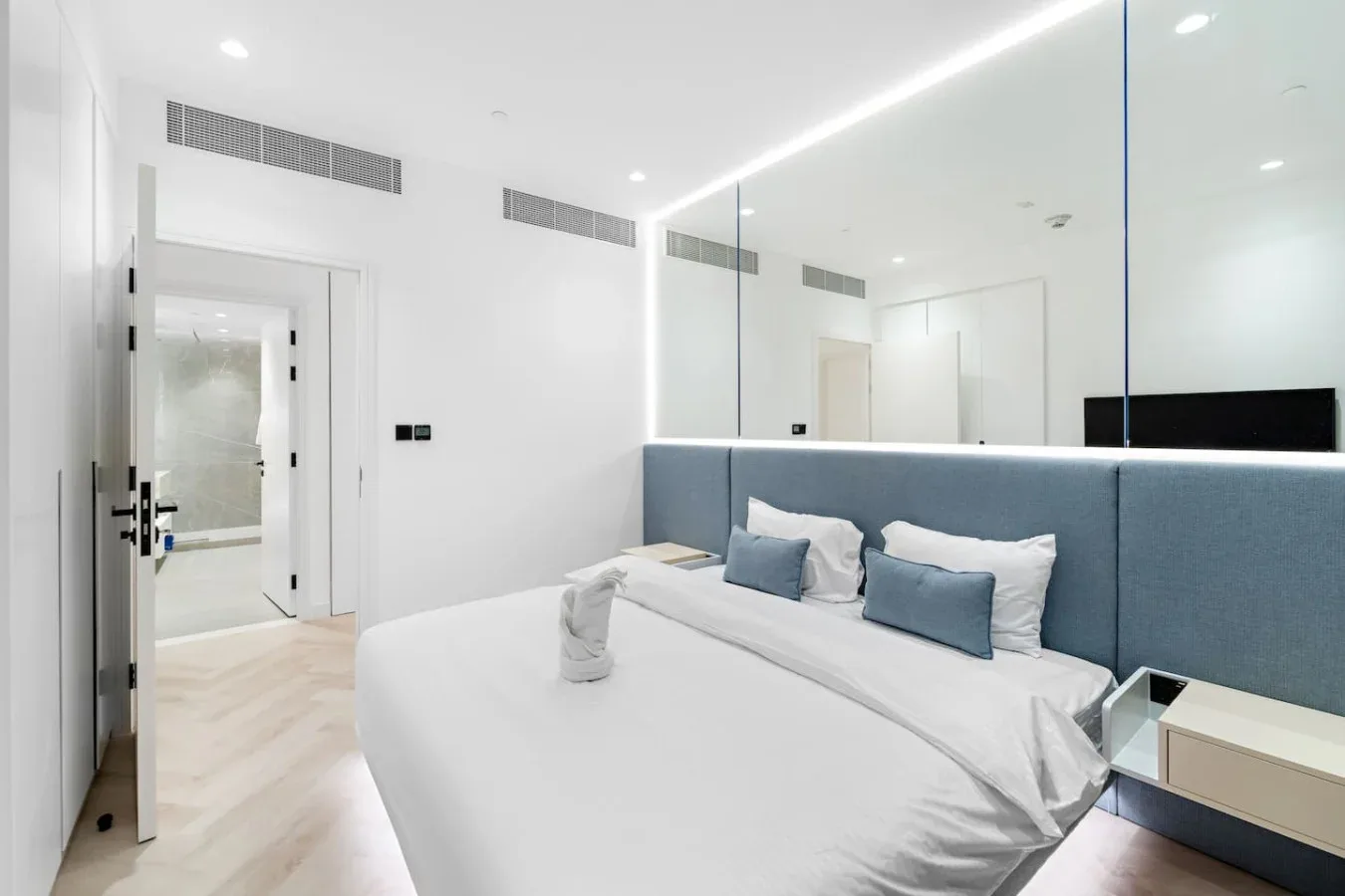 Un dormitorio luminoso con una cama grande y un cabecero azul tapizado.