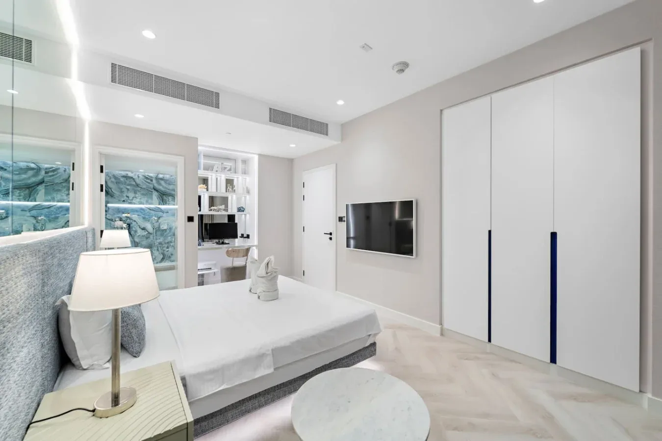 Un dormitorio luminoso con una cama, un televisor en la pared y grandes ventanas.