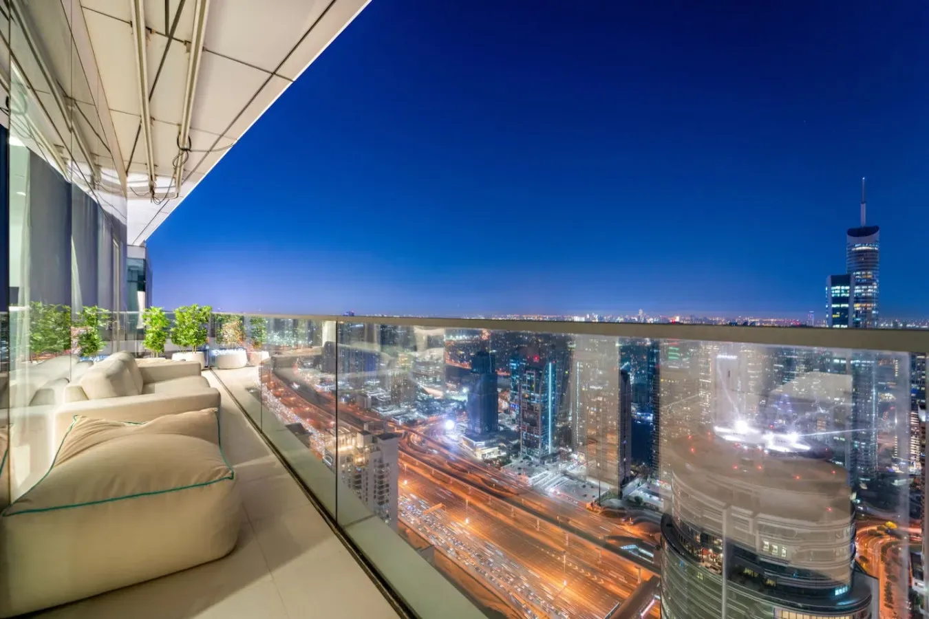 Una zona de estar en un balcón da a edificios y carreteras iluminados por la noche.