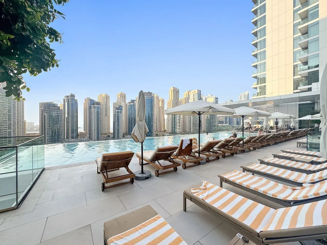 Una terraza con piscina tiene tumbonas y sombrillas frente al perfil urbano.