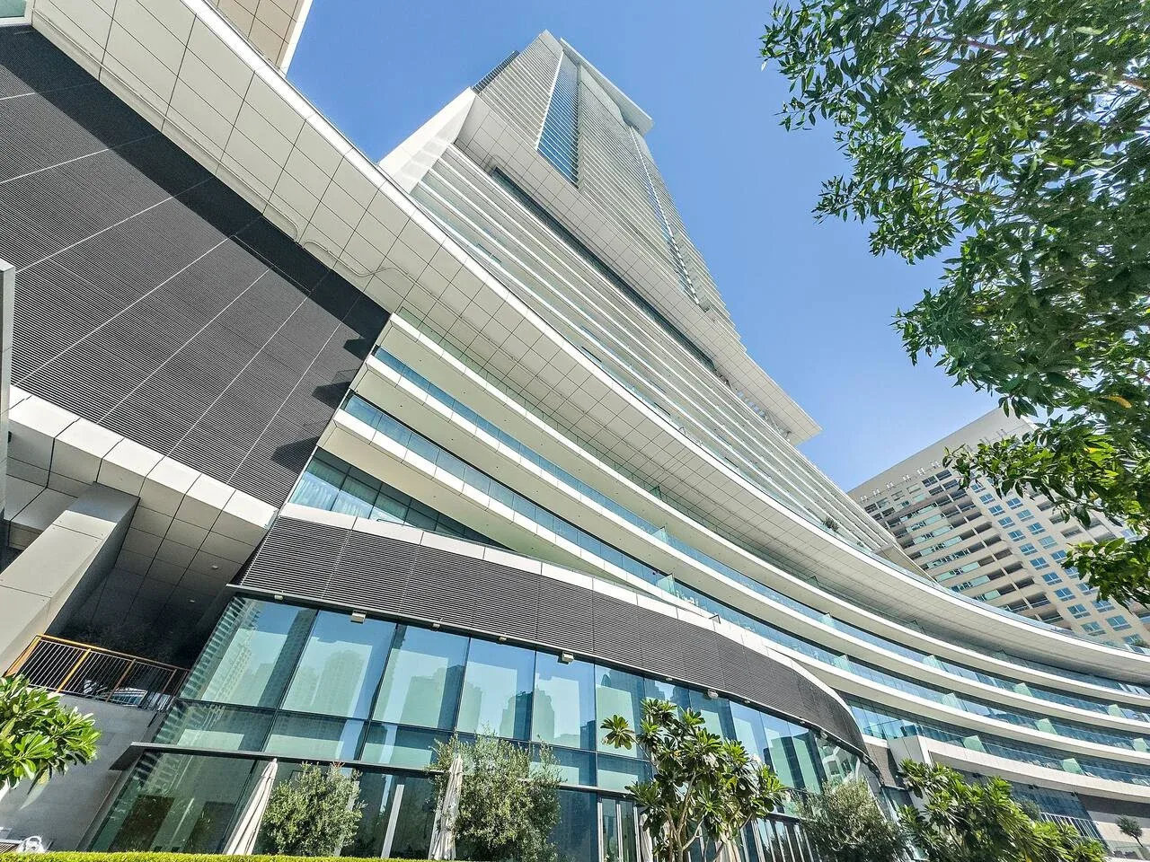 Un edificio moderno de gran altura se eleva sobre un nivel inferior con fachada de vidrio, bajo un cielo despejado.