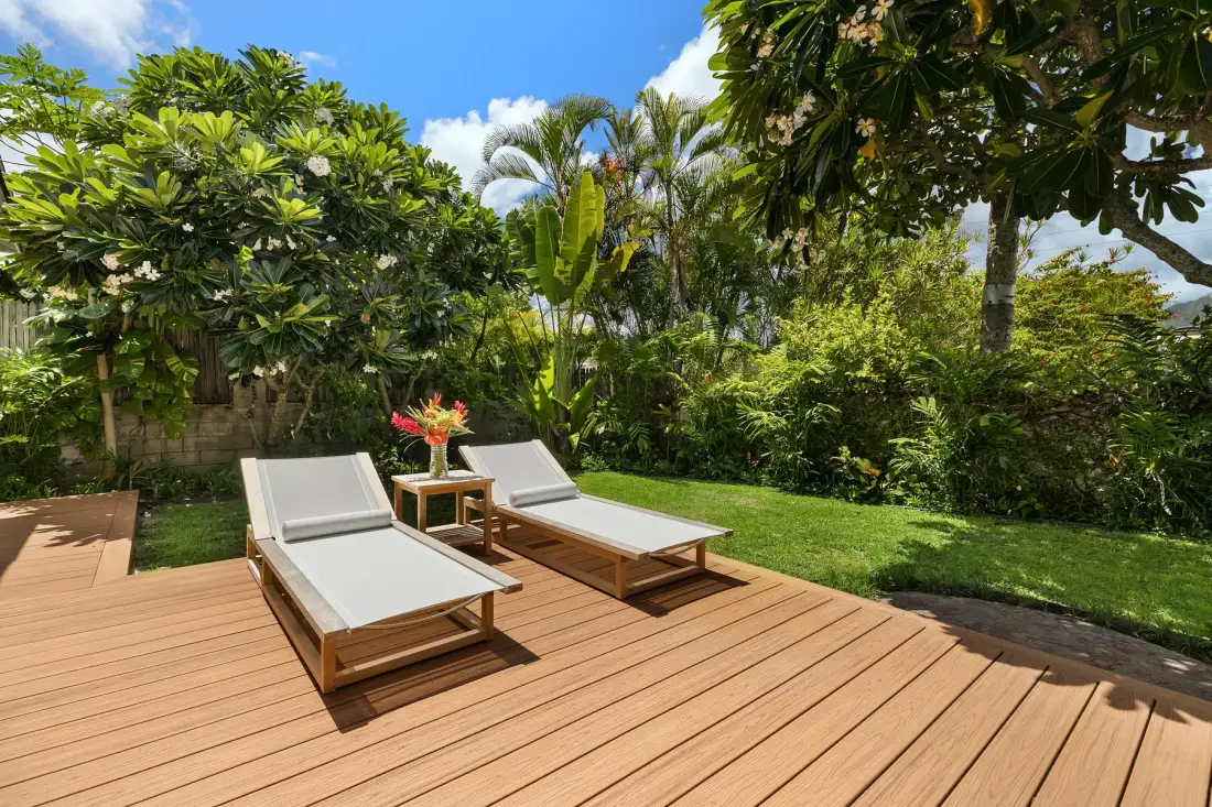 A wooden deck with outdoor loungers overlooks a lush garden.