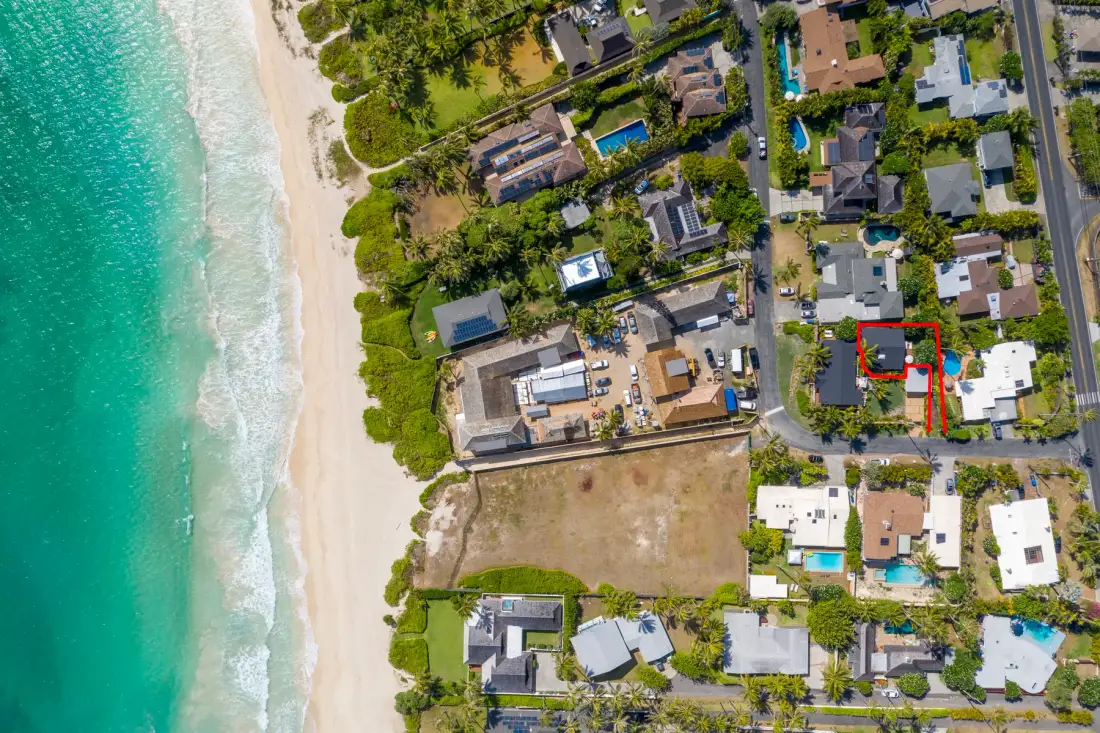 Vista aérea de un barrio junto a la playa, con casas, piscinas y una costa arenosa.