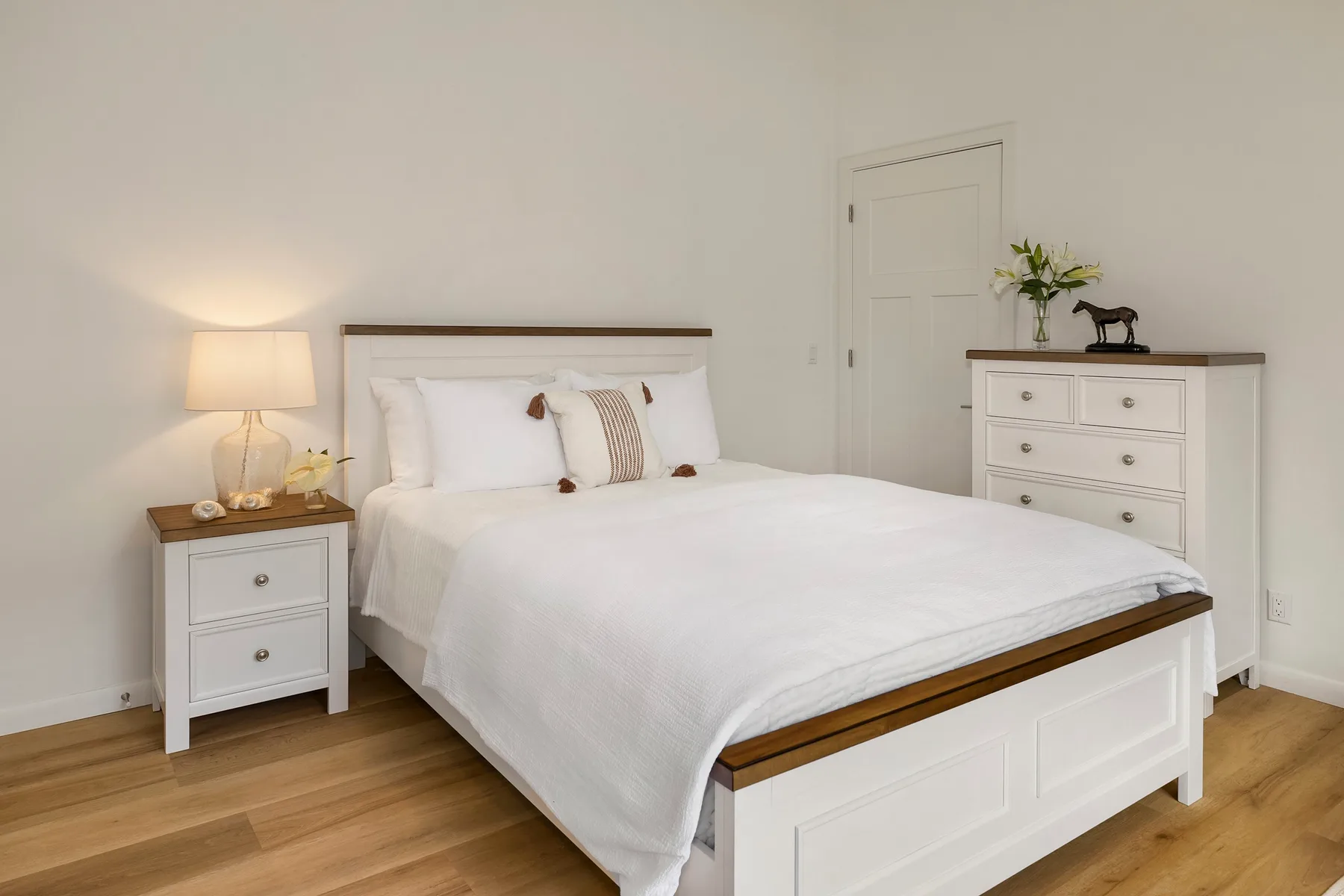 Un dormitorio con una cama bien tendida, una mesita de noche y una cómoda blanca.