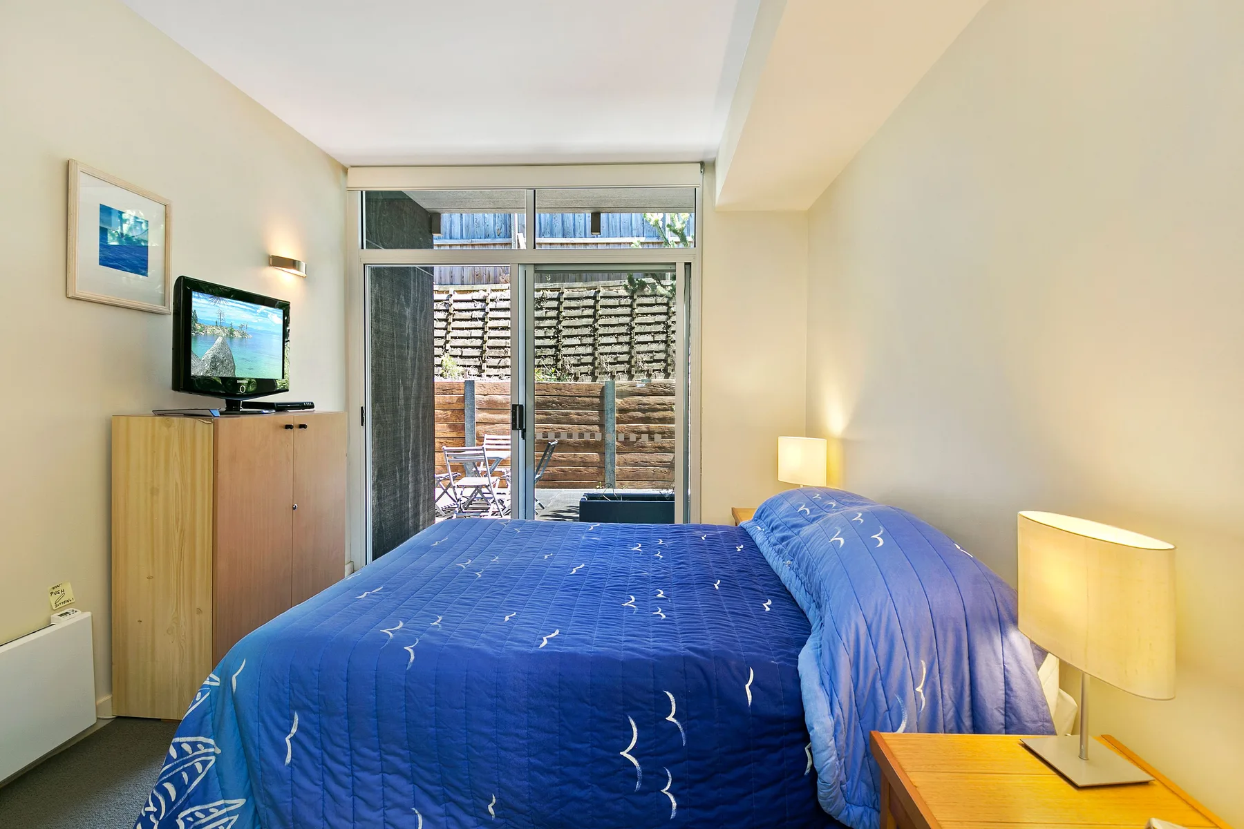Un dormitorio con ropa de cama azul, un televisor y una ventana amplia.