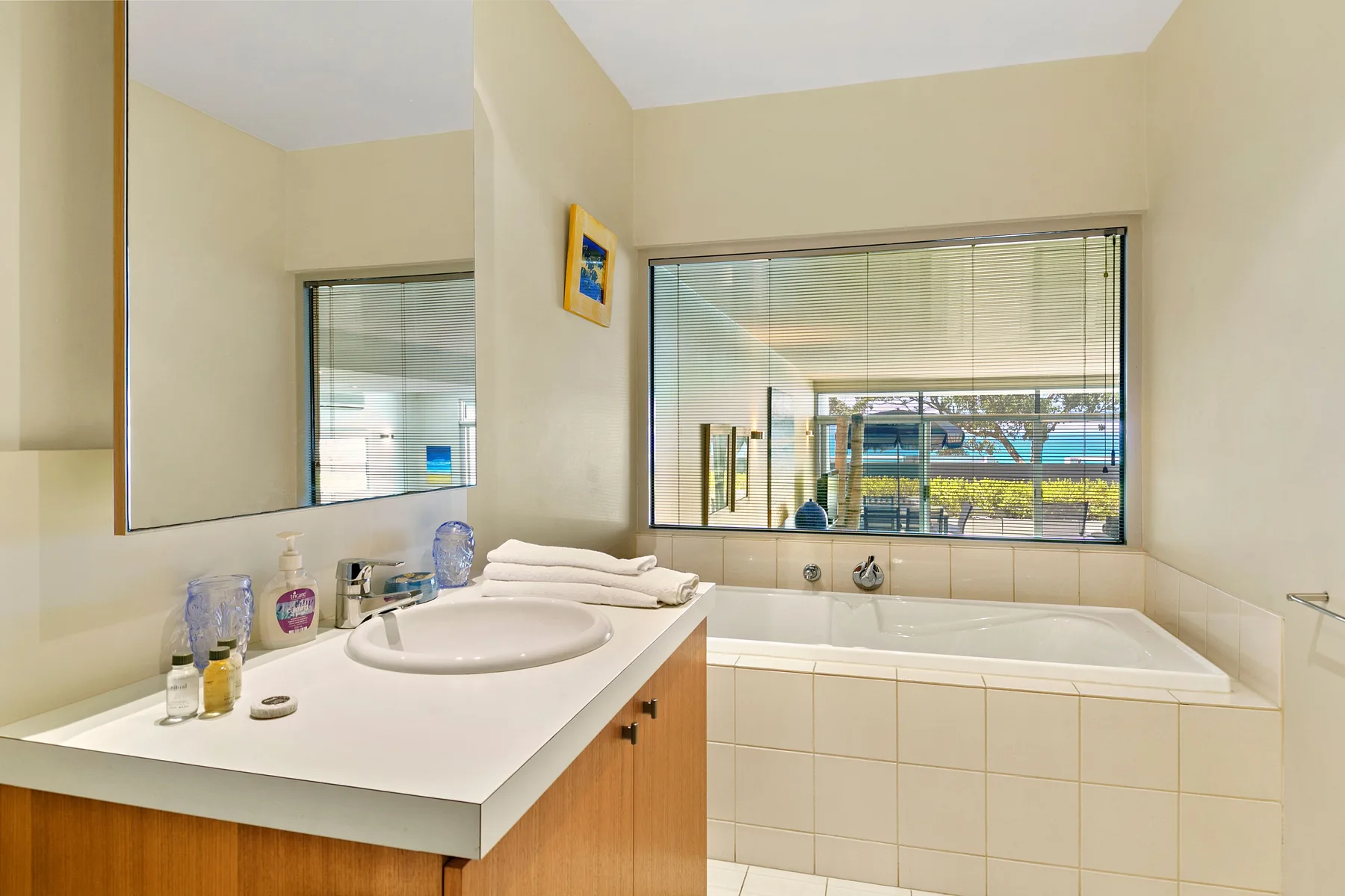 Un baño con lavabo junto a una bañera y ventanas grandes.