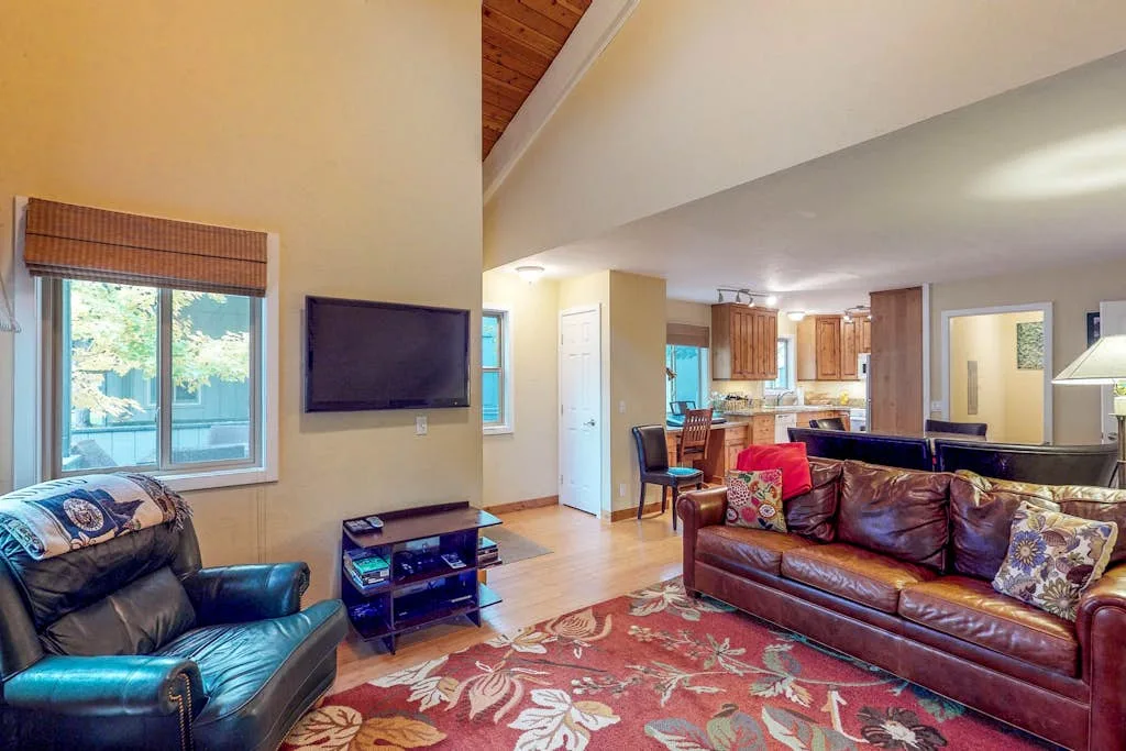 A living room with leather seating, a television, and an open kitchen beyond.