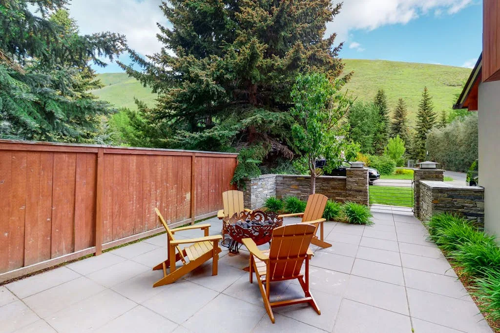 A paved outdoor patio has wooden seating beside a garden and hillside.