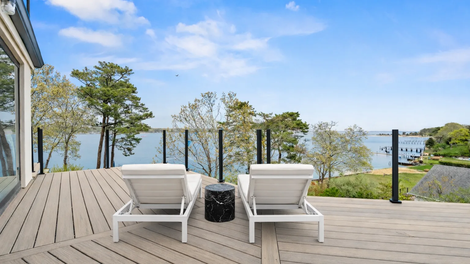 A waterfront deck has two lounge seats facing the water.