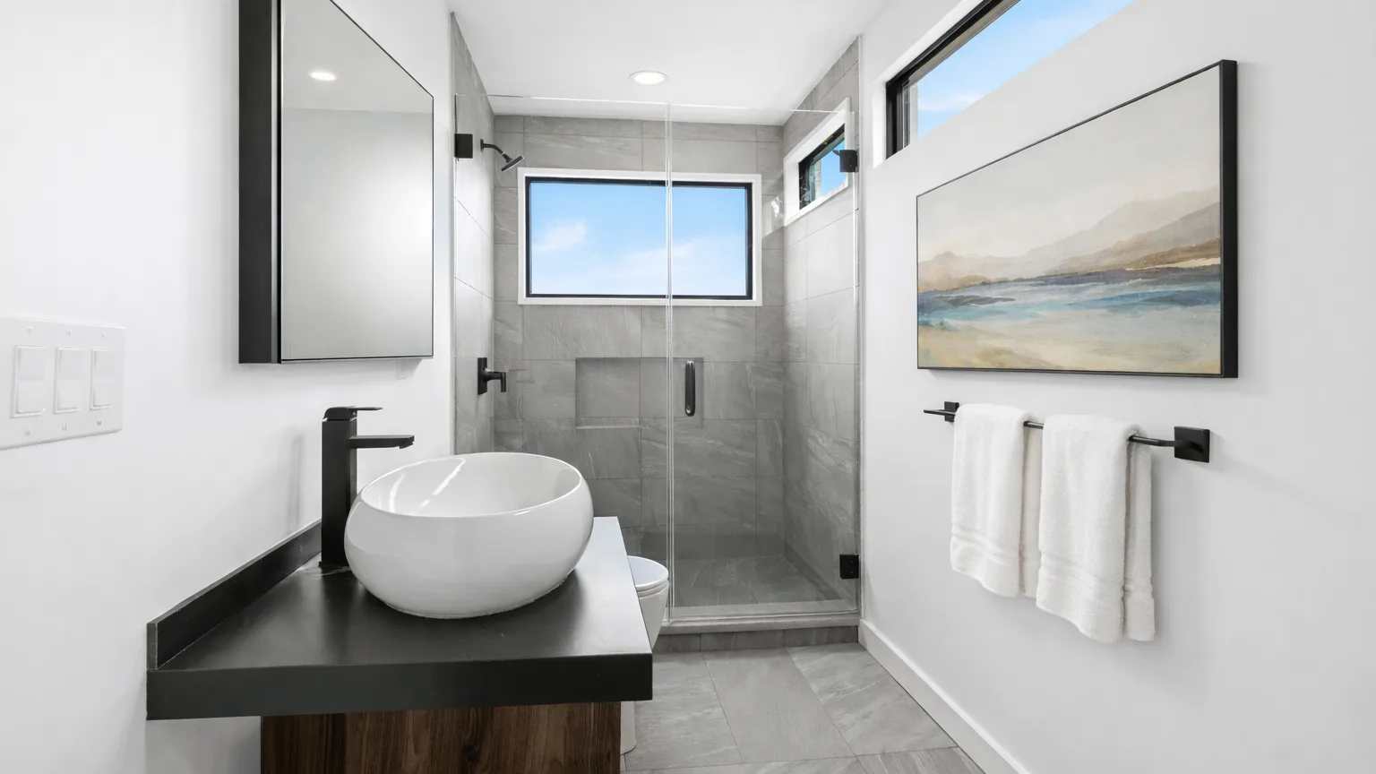 A modern bathroom with a sink, large mirror, and glass shower.