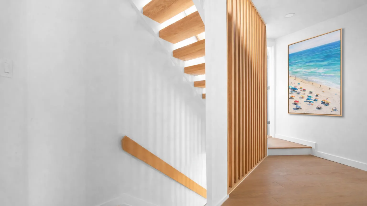 A bright hallway with wooden stairs and a framed beach picture.
