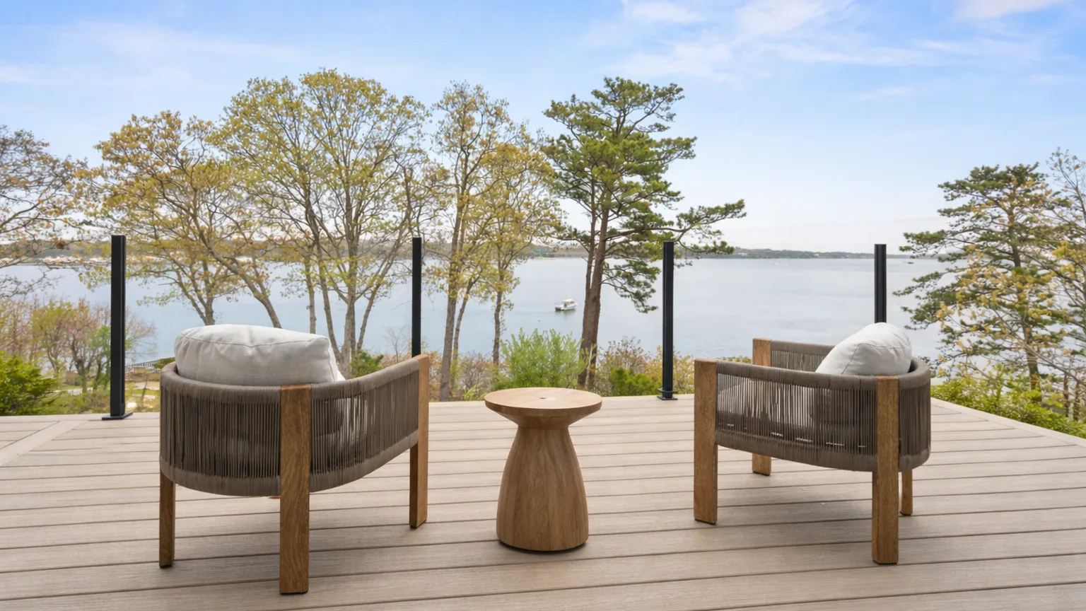 A lakeside deck has two cushioned seats facing the water.