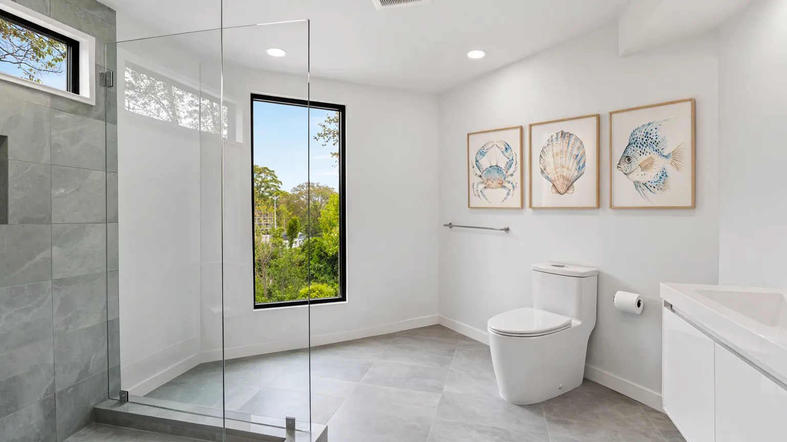 A bright bathroom with a glass shower and framed shell artwork.