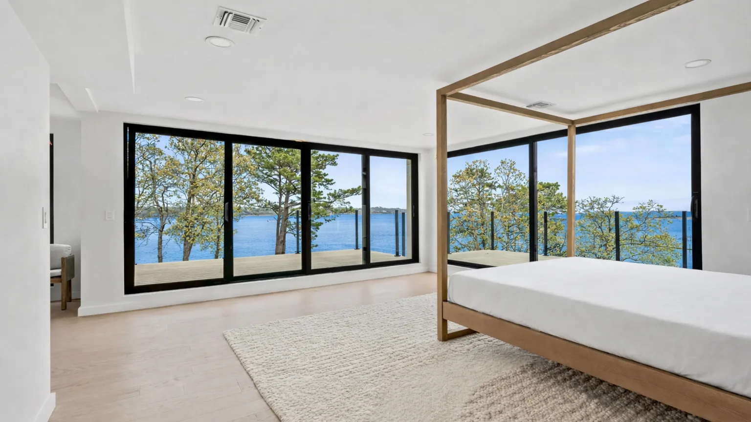 A bedroom with a bed beside large windows overlooking the water.