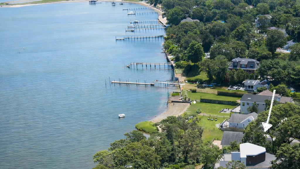 Aerial view of a wooded shoreline with homes, docks, and calm water.
