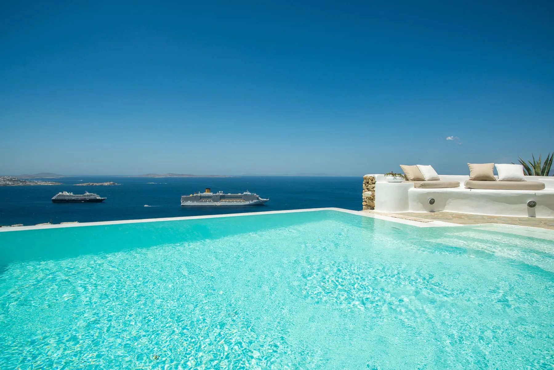 A turquoise infinity pool overlooks the sea, with a built-in seating area beside it.