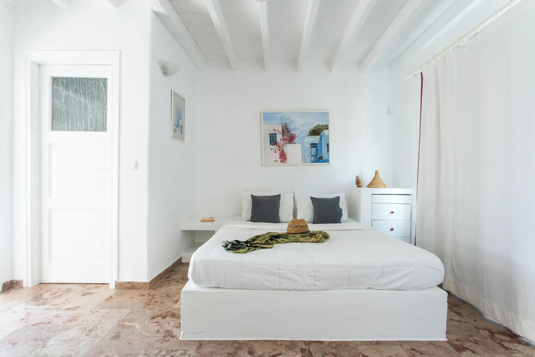 A bright bedroom with a white bed, dark cushions, and wall art.