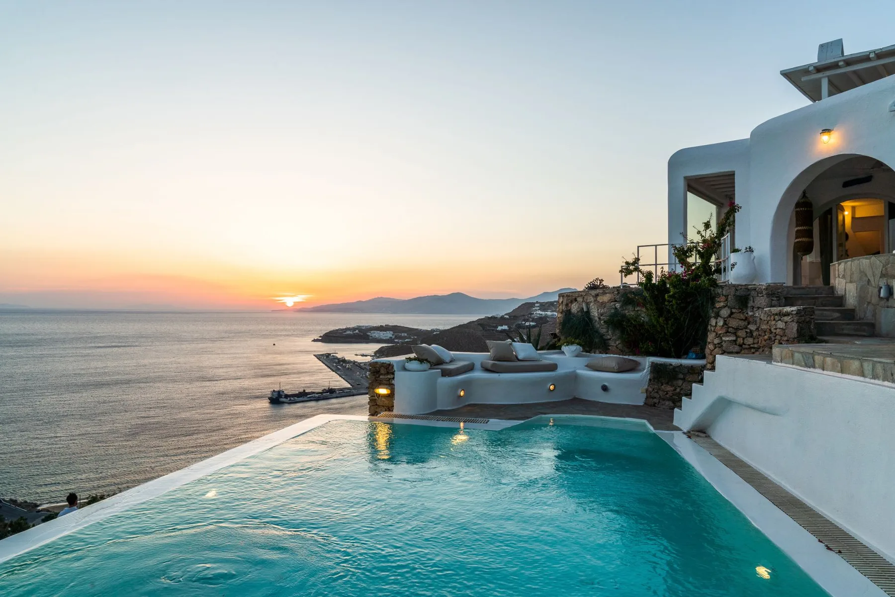 A seaside pool overlooks the water at sunset beside a white building.
