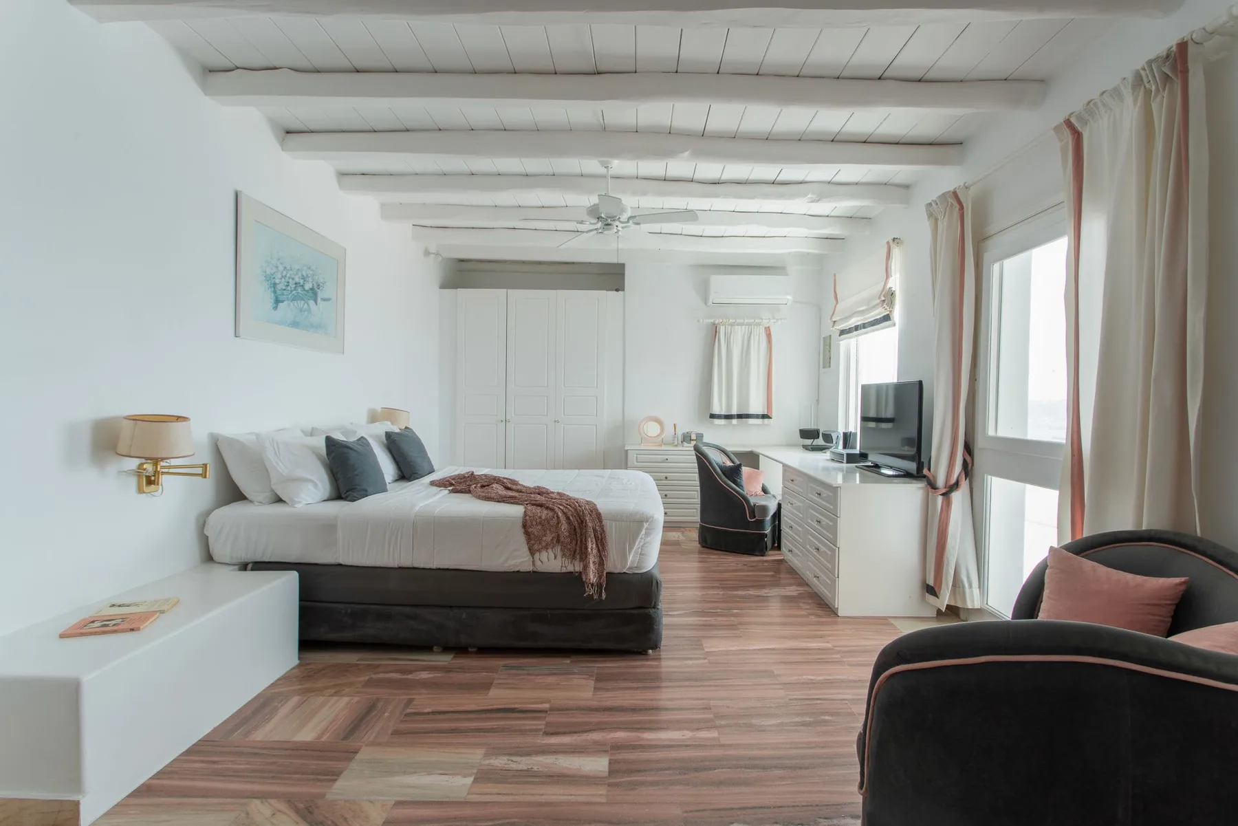 A bright bedroom with a bed, desk, and large windows.