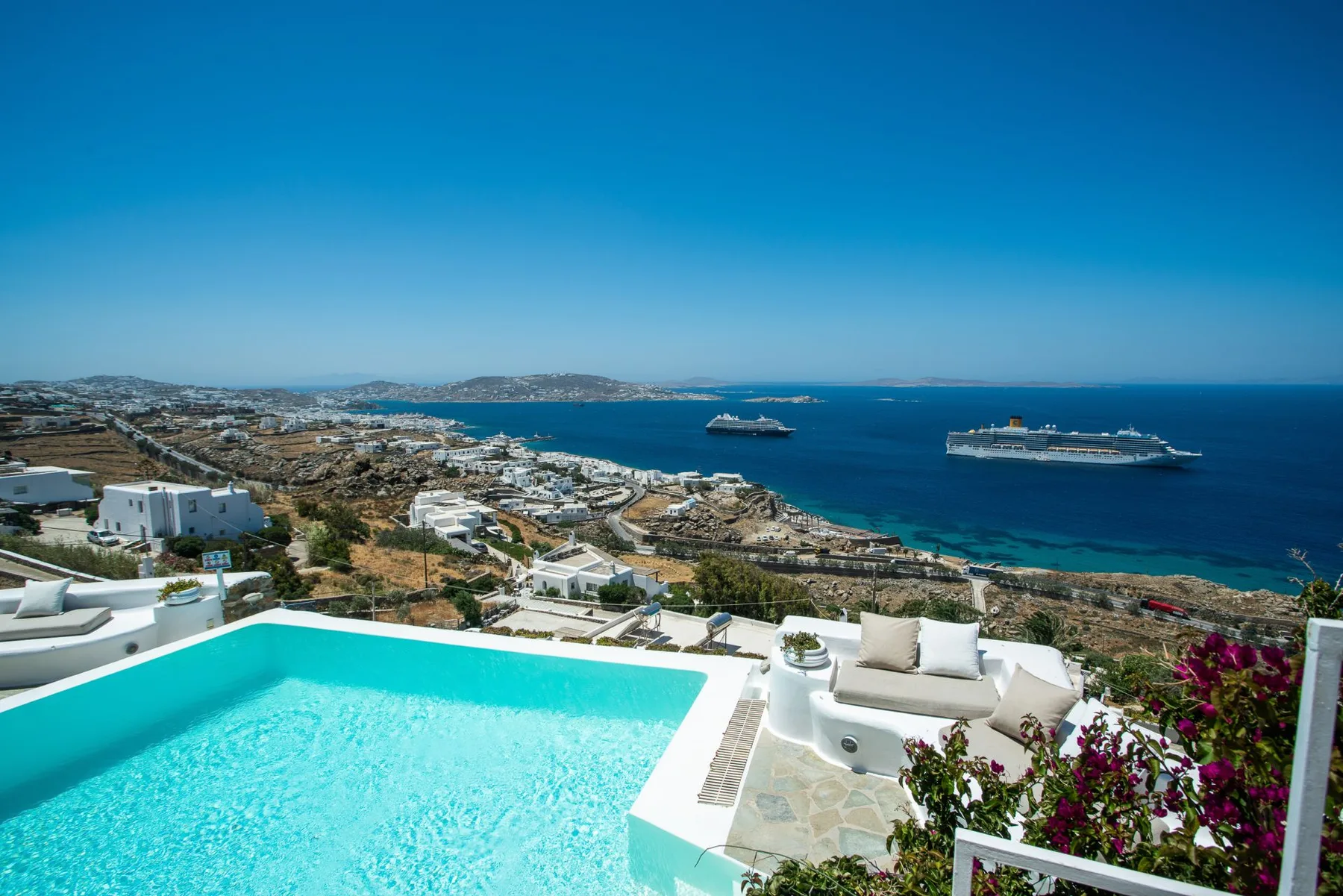 A terrace pool overlooks the coastline and cruise ships on the sea.