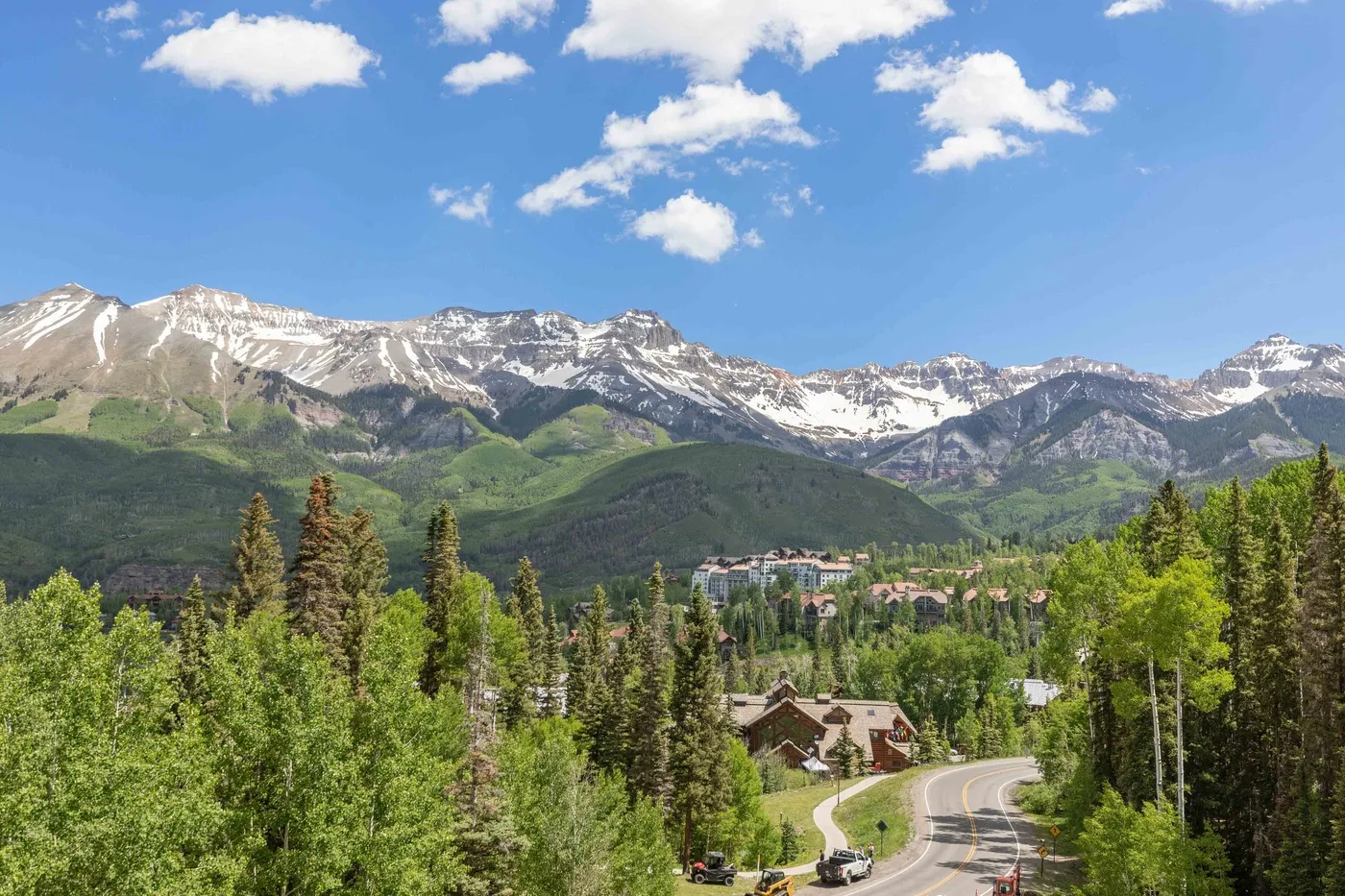 Una carretera sinuosa atraviesa un bosque verde bajo montañas nevadas.