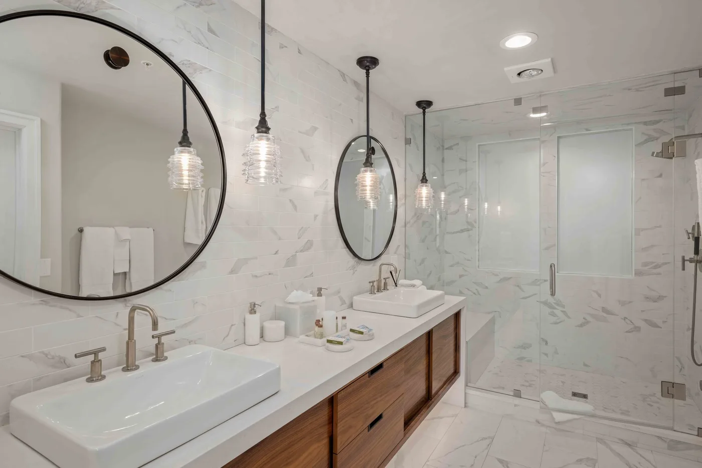 Un baño luminoso de mármol con un tocador largo y una ducha de vidrio.