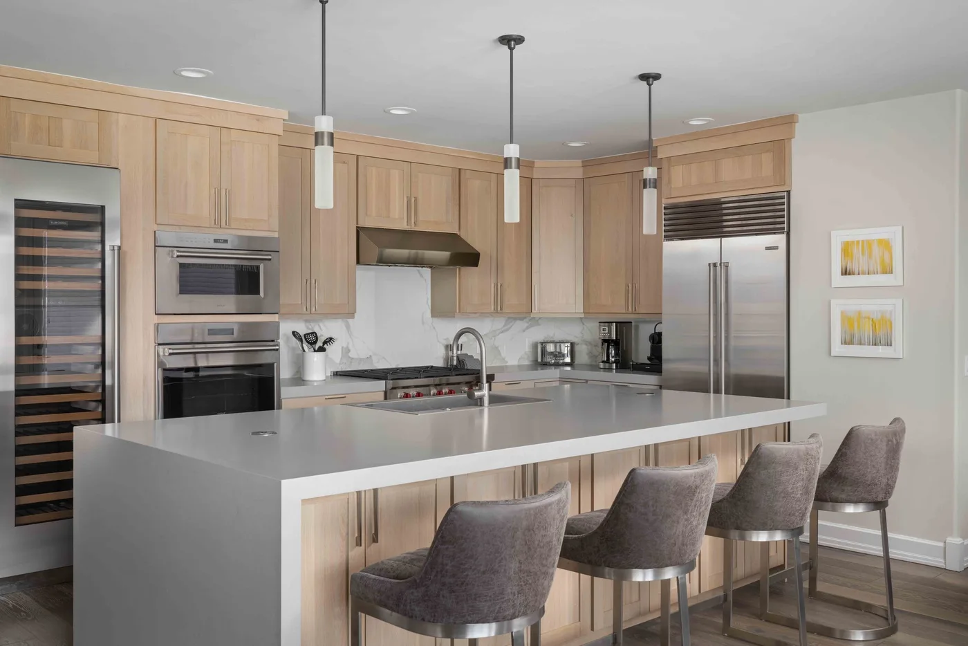Una cocina luminosa con una isla grande, gabinetes de madera clara y electrodomésticos de acero inoxidable.