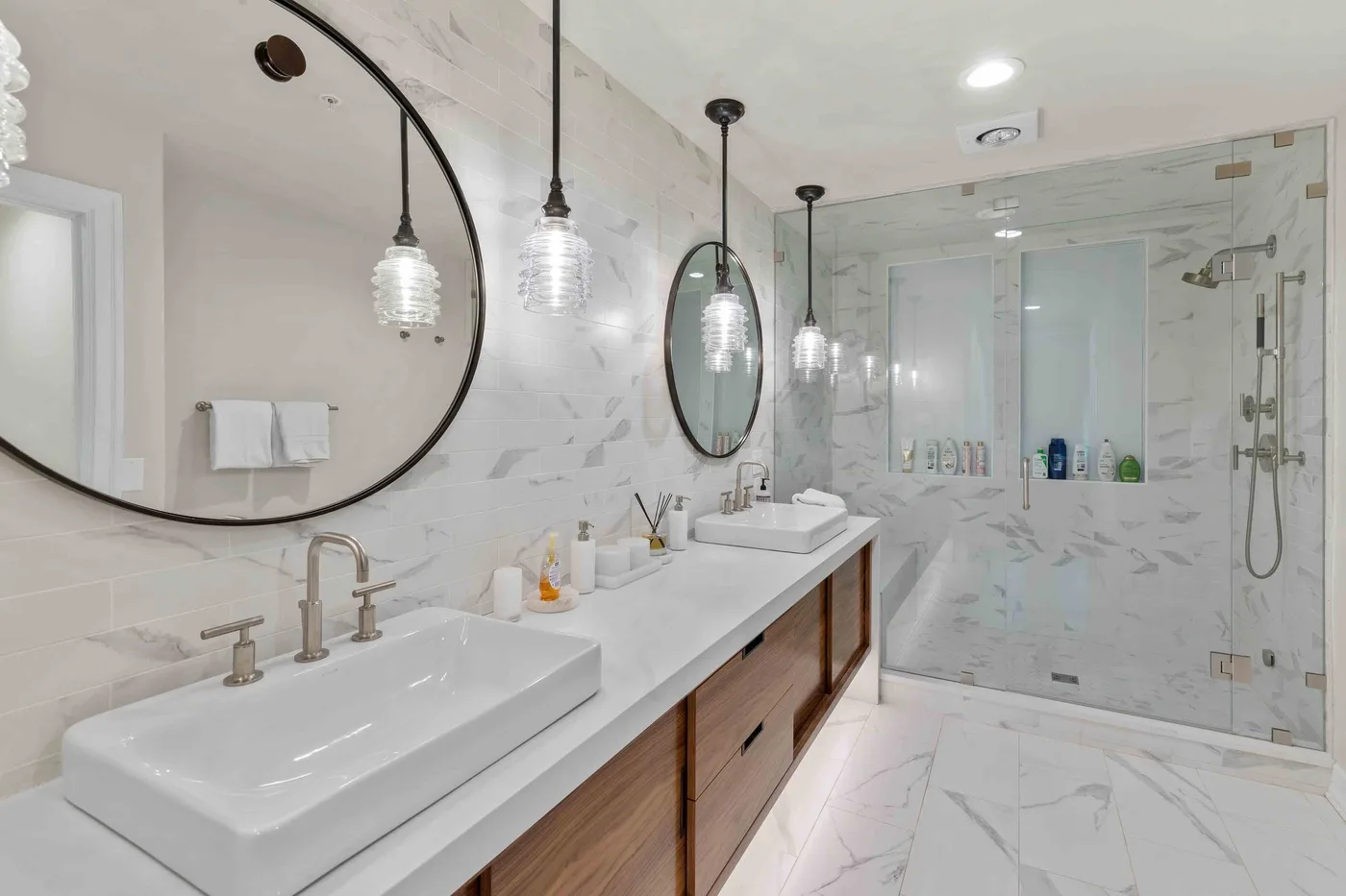 Un baño luminoso con un tocador largo, lavabos sobre encimera y una ducha de vidrio.