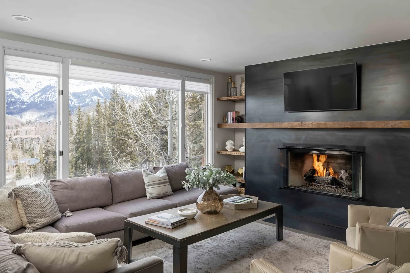 A living room with seating, a fireplace, and large windows overlooking a mountain landscape.