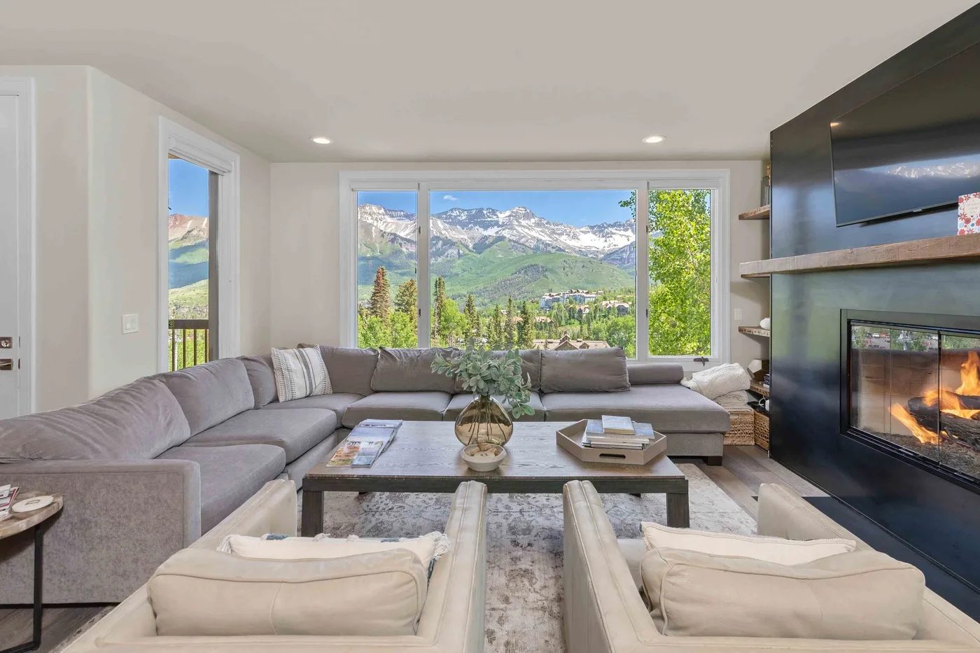Una sala luminosa con asientos seccionales, chimenea y vistas a las montañas por amplias ventanas.