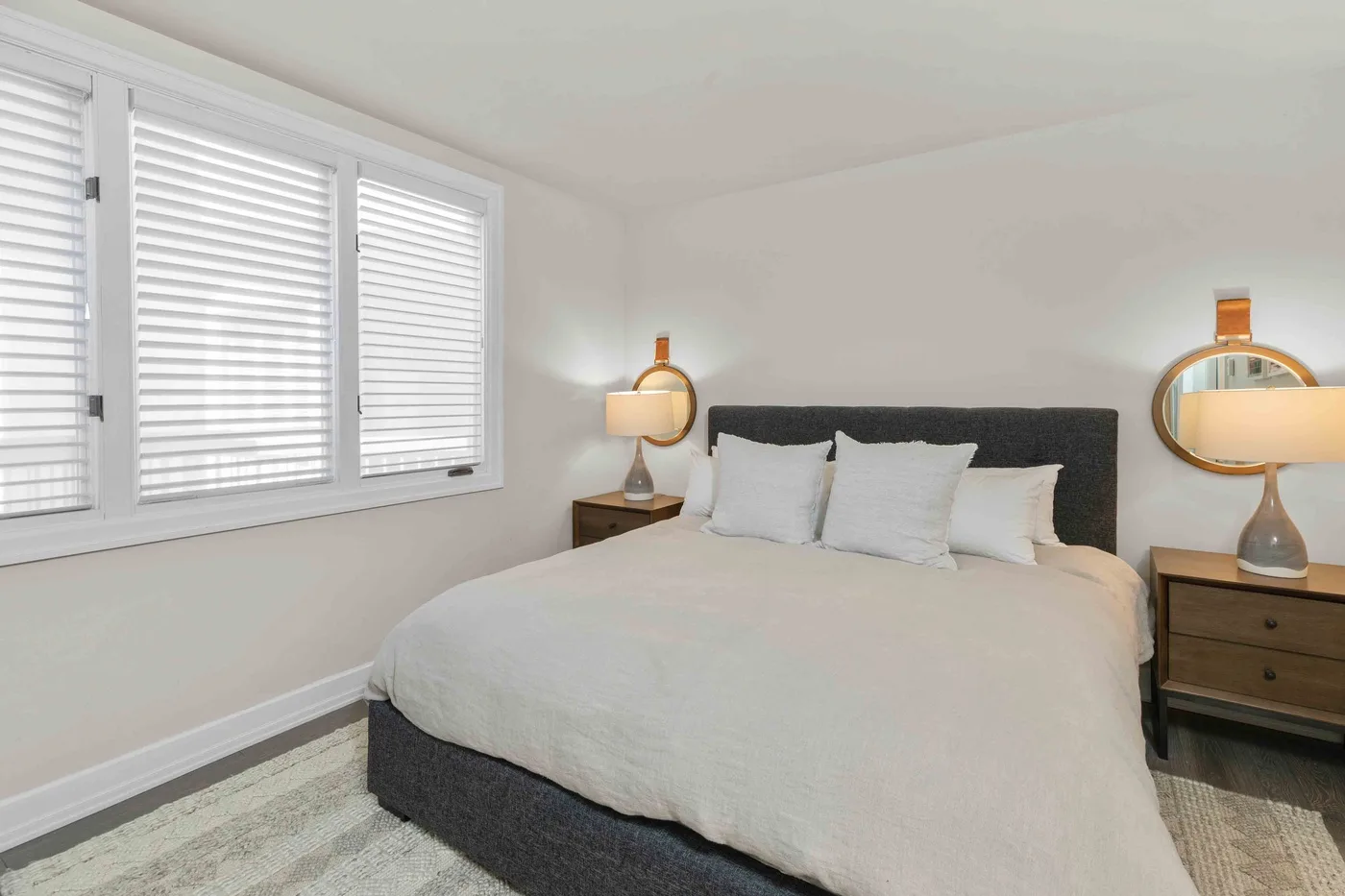 Un dormitorio con cama, mesas de noche y ventanas con persianas.