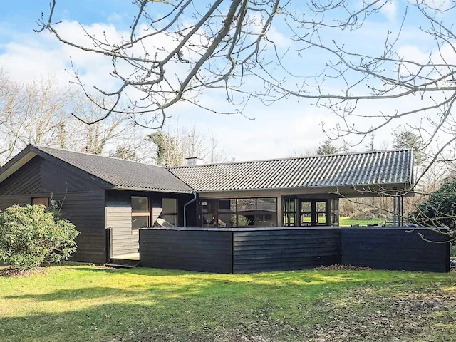 Casa de una planta con exterior oscuro y un patio cercado con césped.