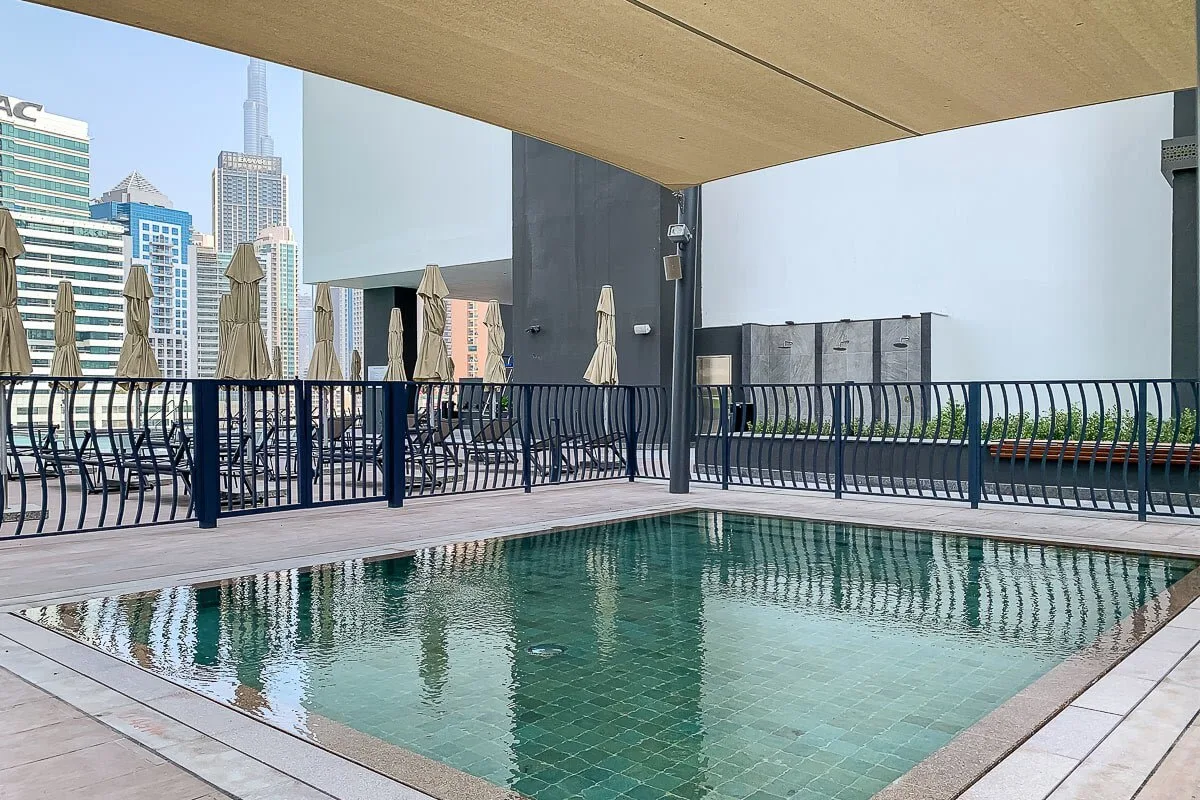 Una piscina en la azotea está junto a una terraza, con edificios de la ciudad al fondo.