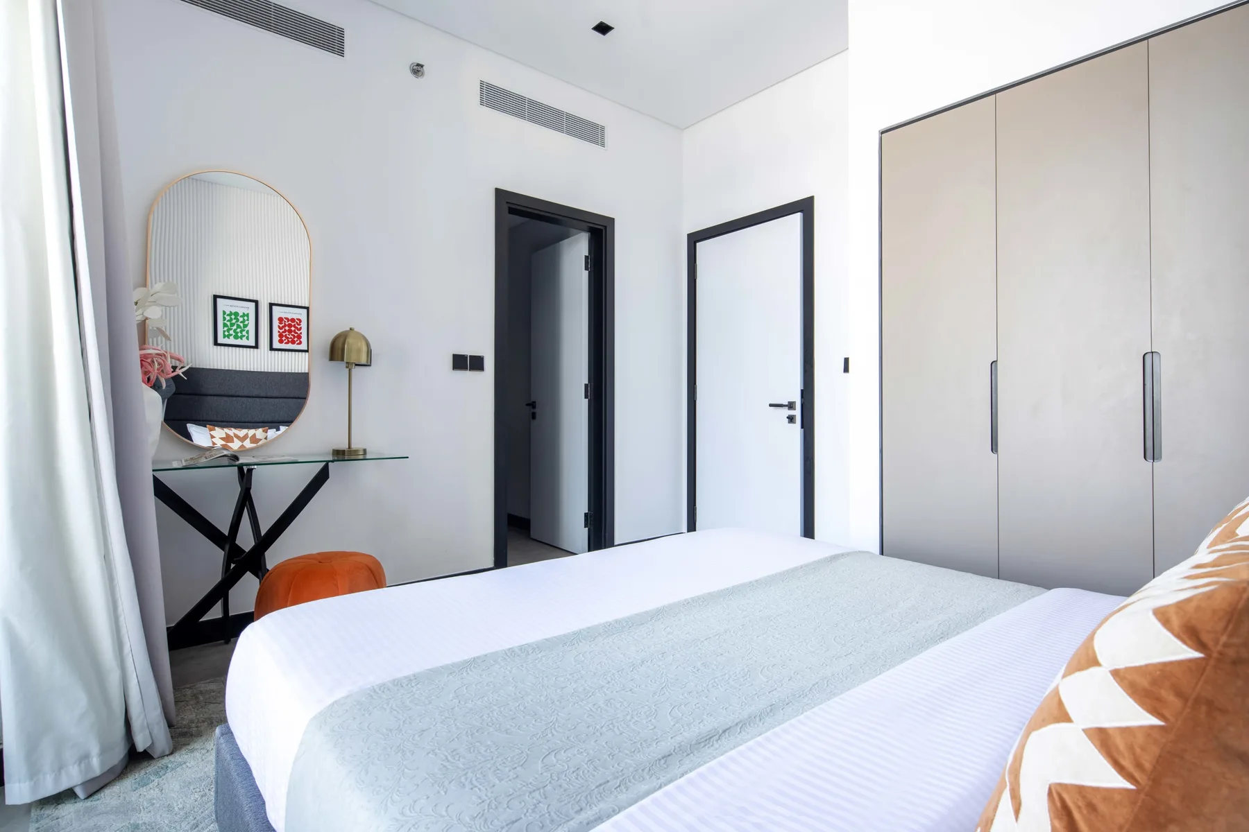 Un dormitorio luminoso con una cama tendida y un armario junto a la pared.
