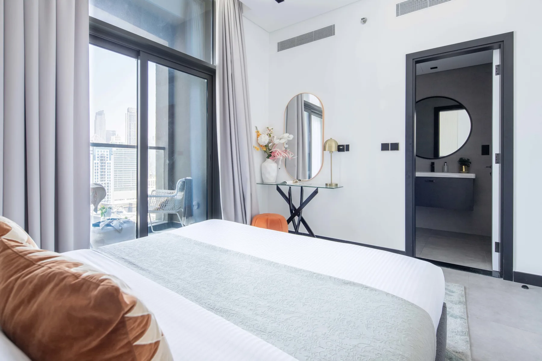 Un dormitorio con una cama junto a una ventana grande con vistas a edificios.