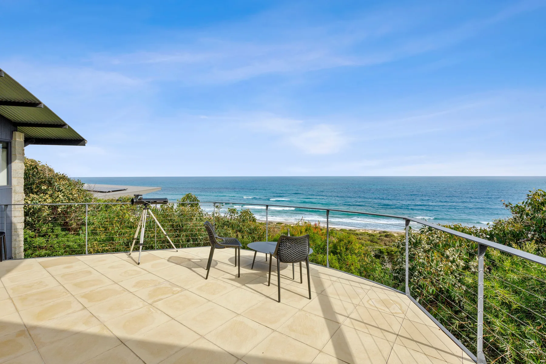 A tiled outdoor terrace overlooks the ocean, with a small table and seating.