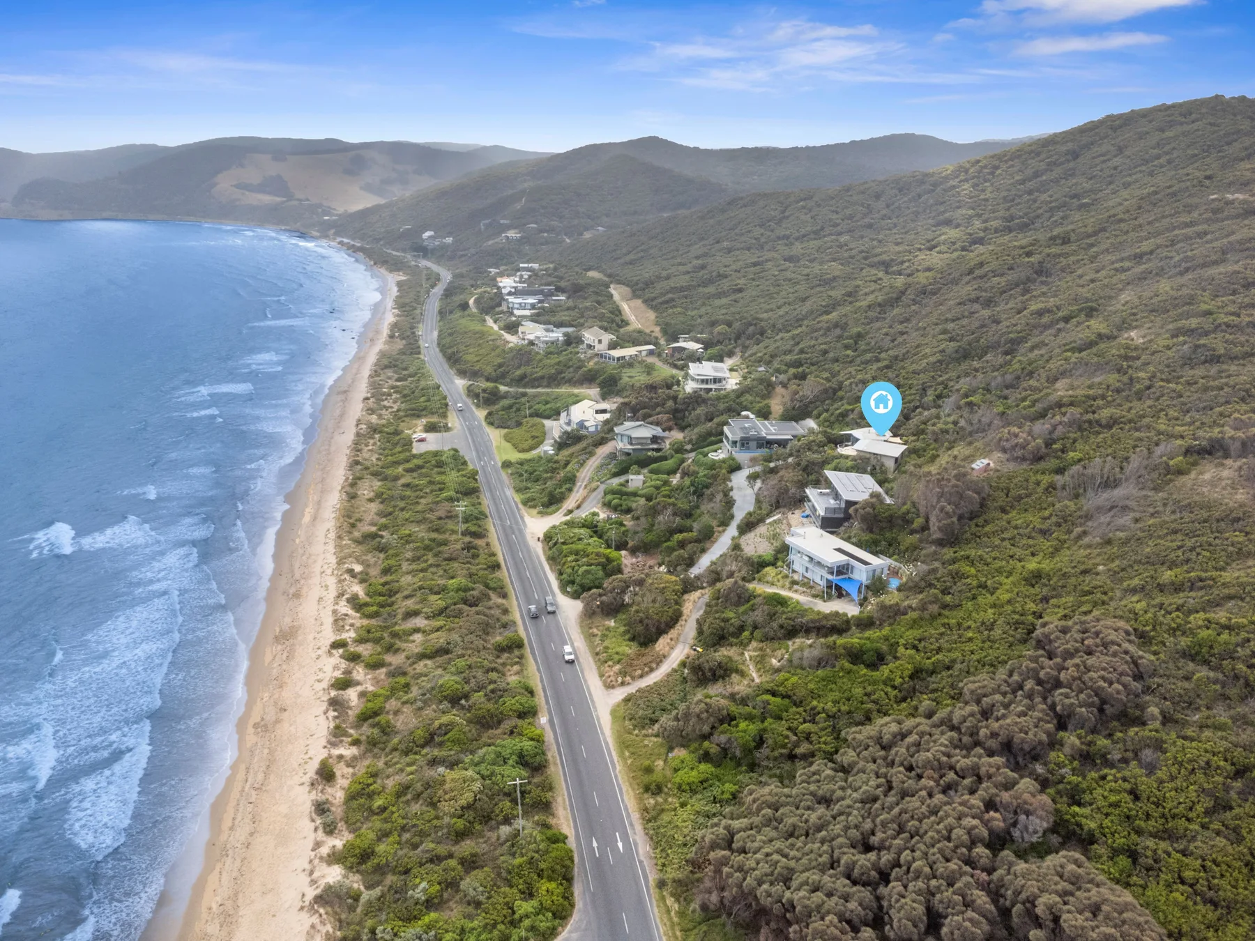 Aerial coastal landscape with a winding road between the beach and hills.