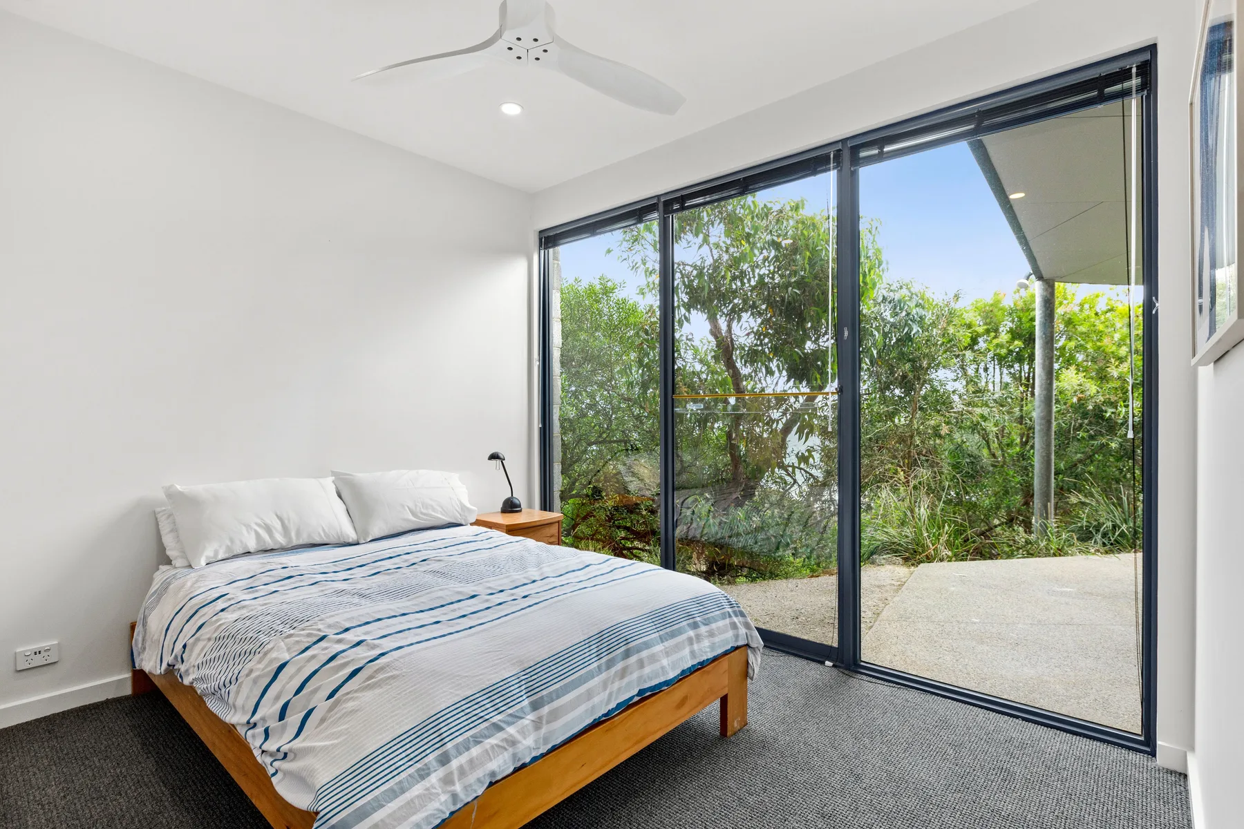 A bedroom with a bed beside large sliding glass doors overlooking greenery.