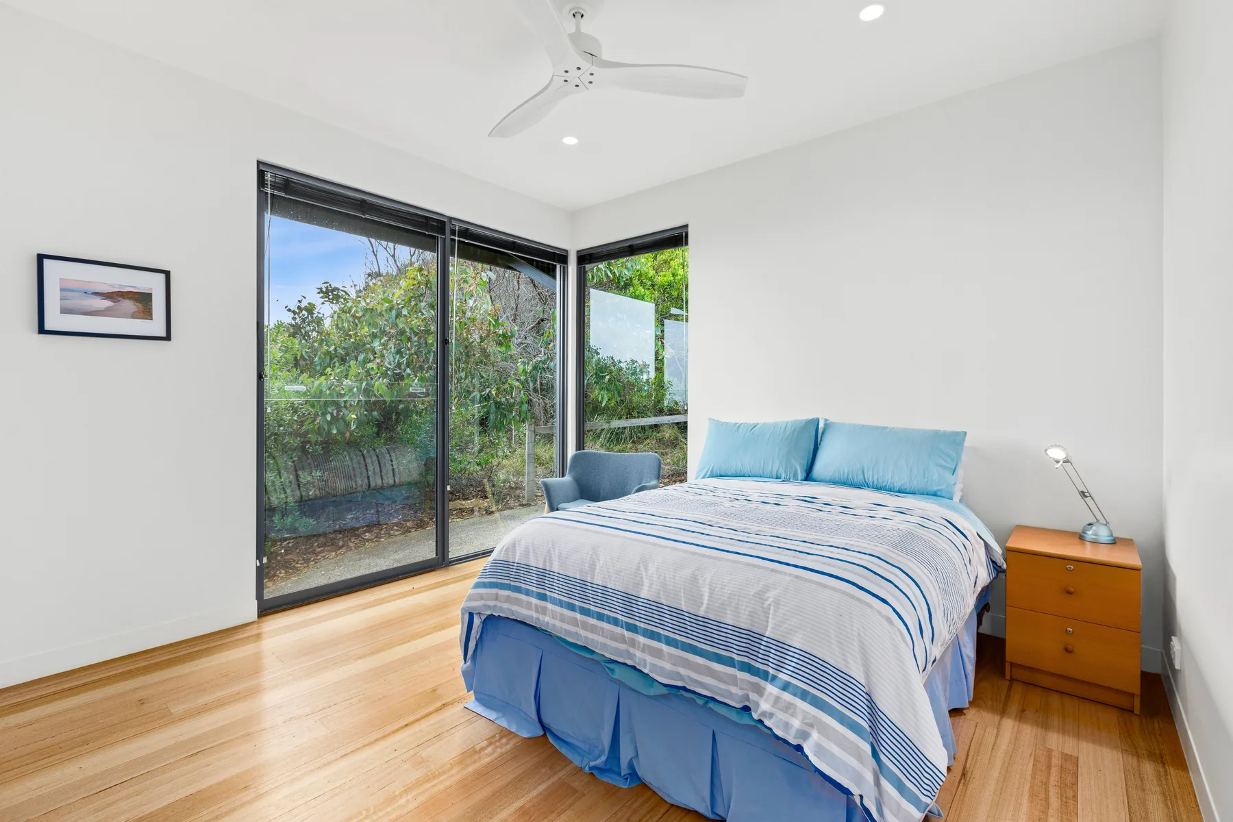 A bright bedroom with a bed beside large windows overlooking greenery.