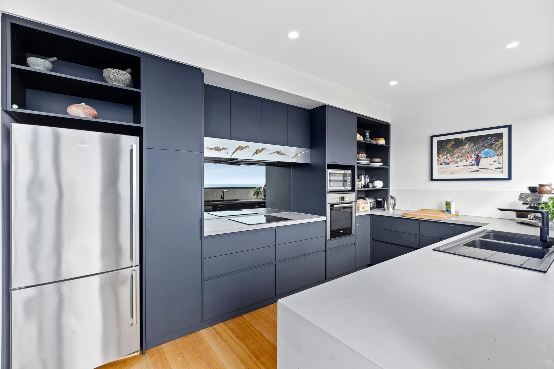 A modern kitchen with dark cabinetry, stainless steel appliances, and a wide island.