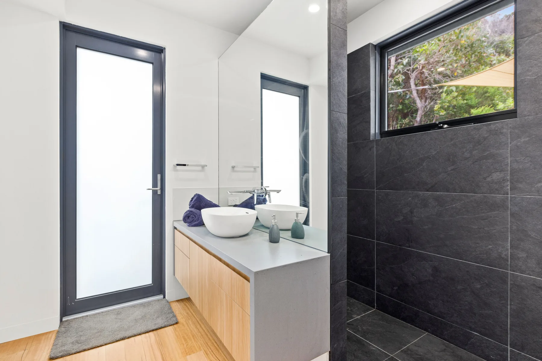A bright bathroom with a double vanity and a dark tiled shower area.
