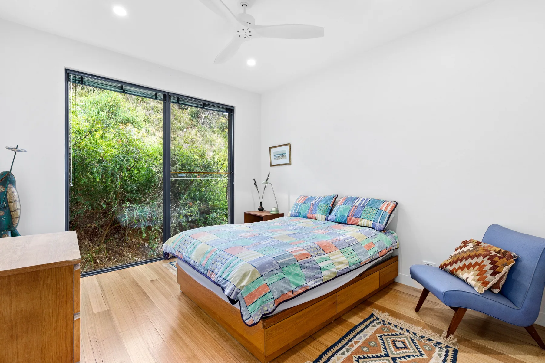 A bright bedroom with a colorful bed beside a large glass door.