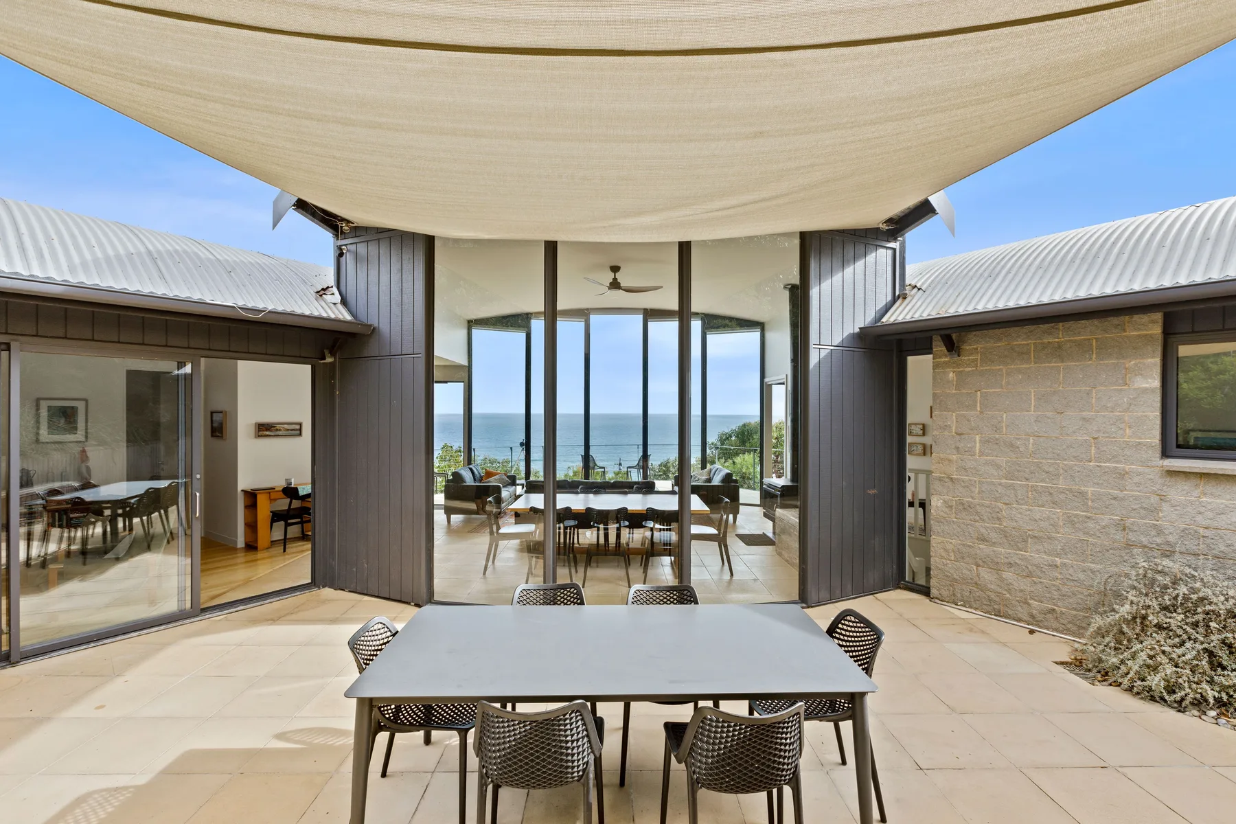 An outdoor dining area faces a glass-walled room with ocean views.