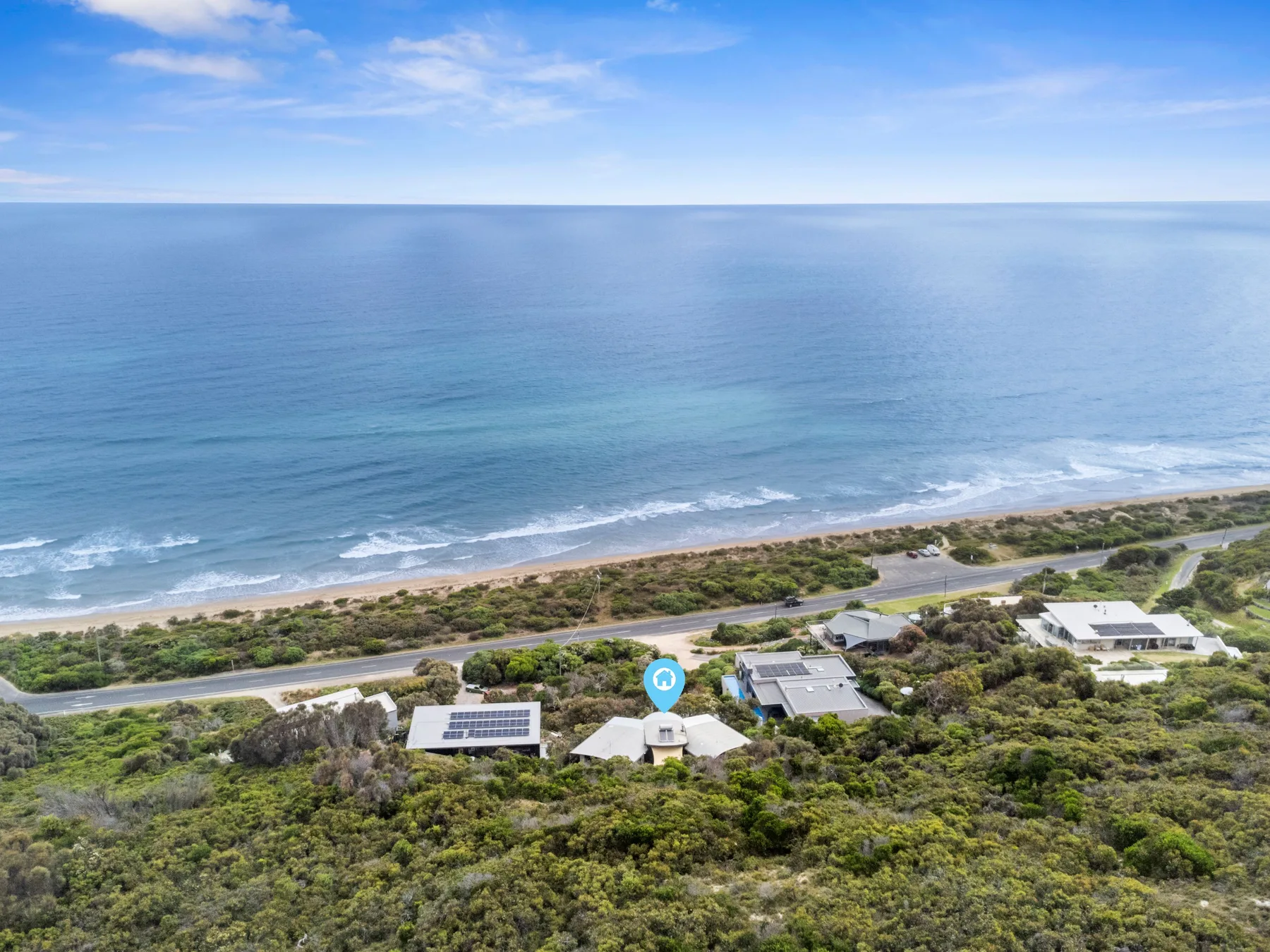 Aerial view of a coastal property among greenery beside the beach and ocean.