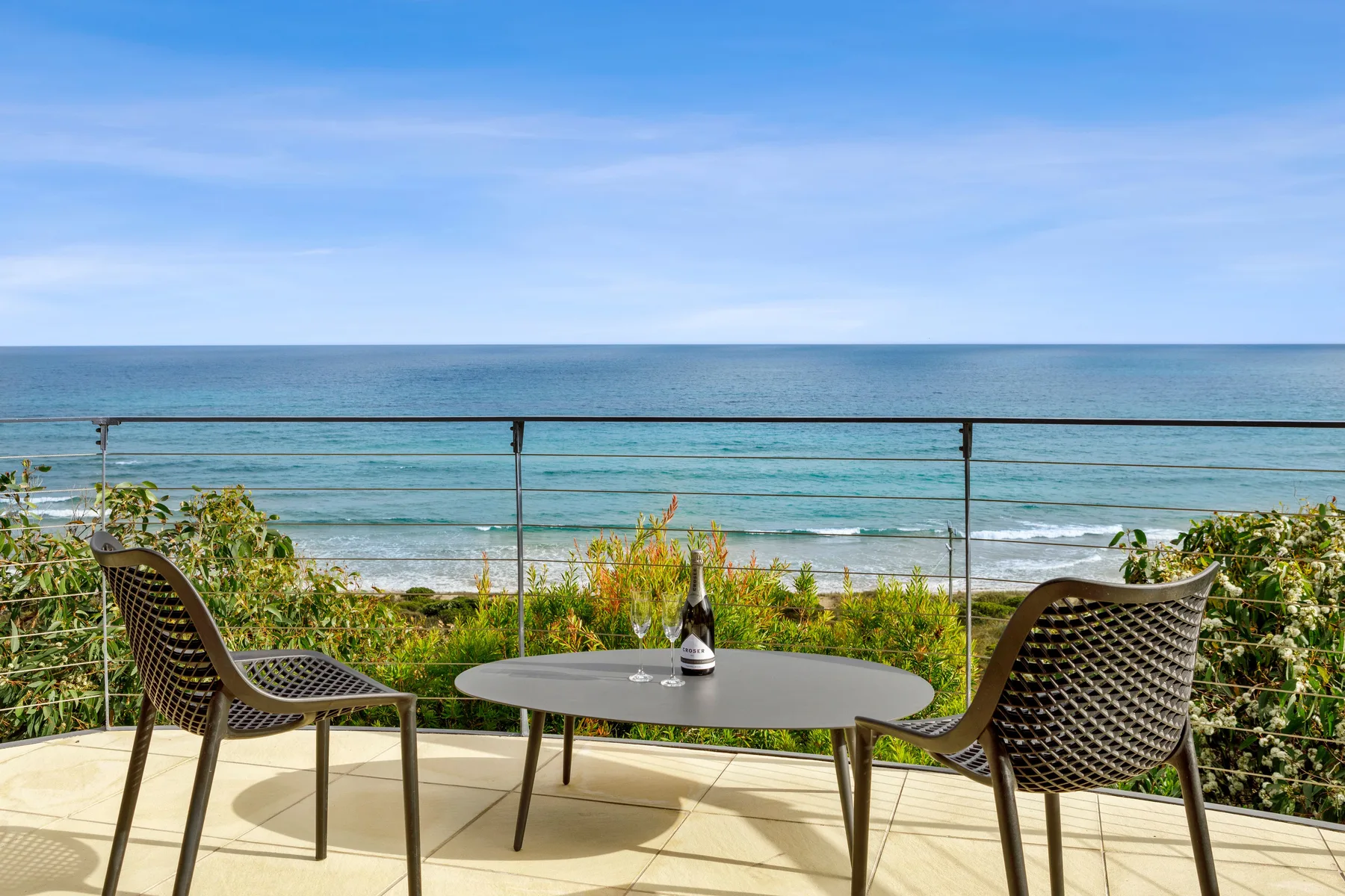 A seaside terrace with seating and a table overlooking the ocean.