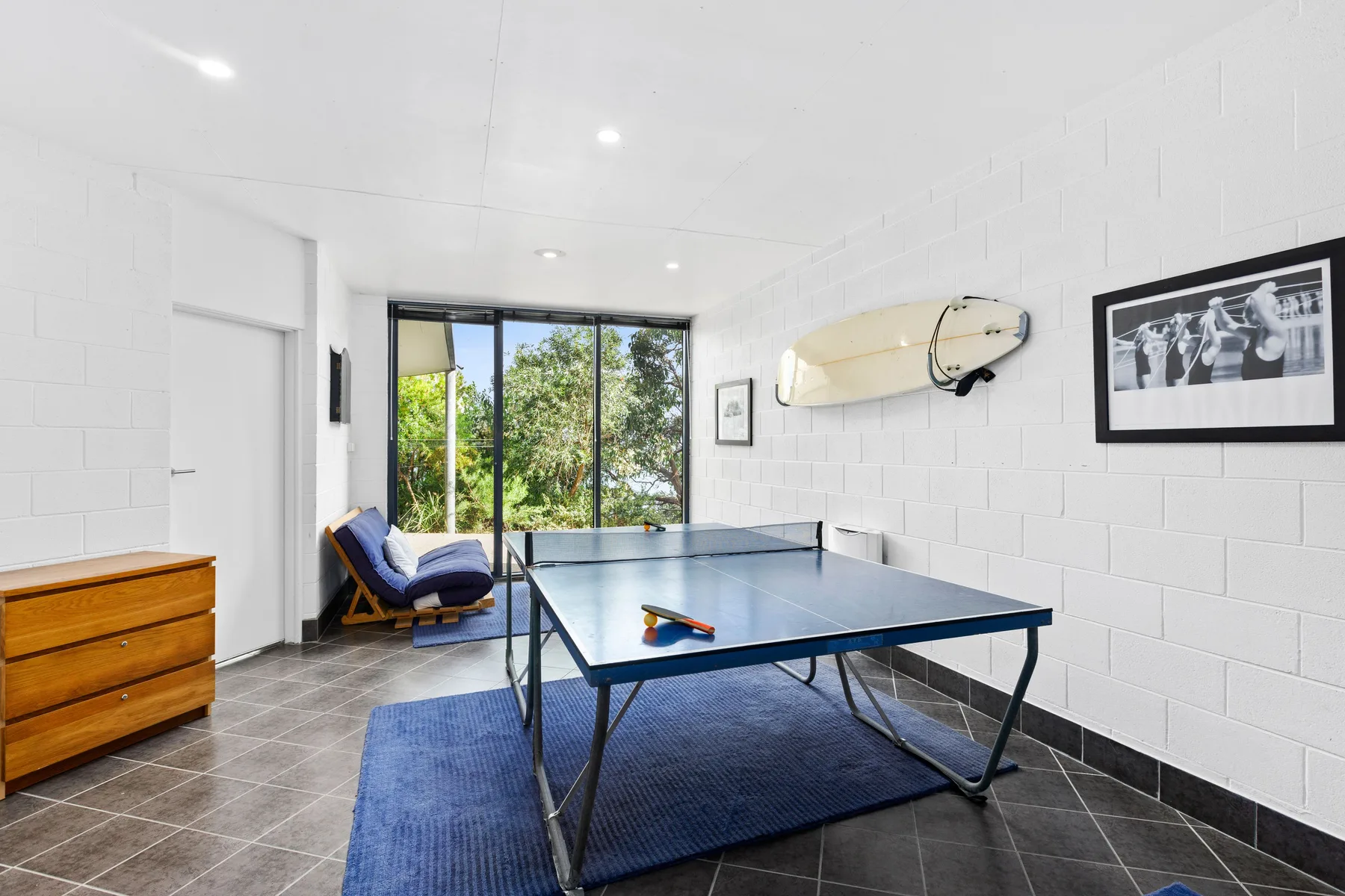 A bright indoor recreation room features a table tennis table and blue rug.